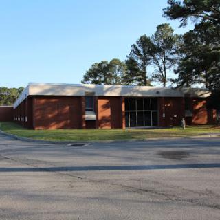 A view of a brick building surrounded by trees, located near a road.