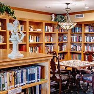 A cozy library with wooden bookshelves, a reading table, and chairs under a decorative chandelier.