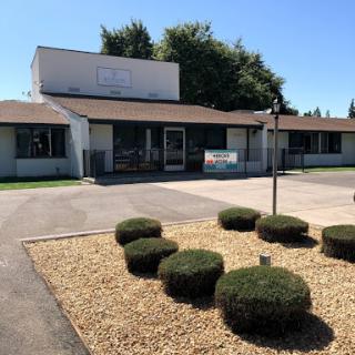 A view of a commercial building surrounded by landscaped bushes and trees on a clear day.