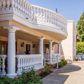 A large house featuring a grand balcony with ornate columns and a garden-lined driveway.