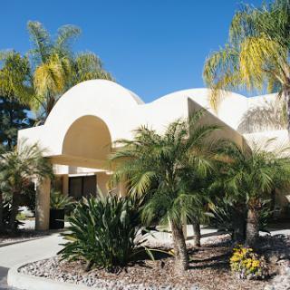 A beautiful, modern building surrounded by lush palm trees and vibrant landscaping under a clear blue sky.