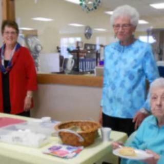 A group of elderly women gathered indoors around a table.