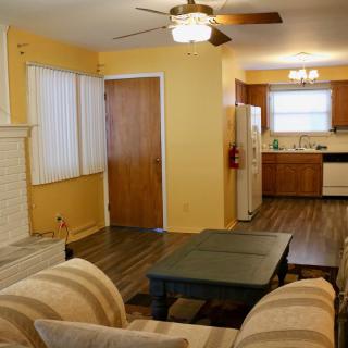 Cozy living room with a view into the kitchen, featuring comfortable seating and a ceiling fan.