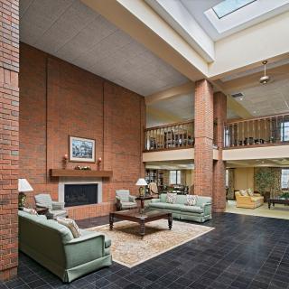Spacious living room with a brick wall, featuring a fireplace and comfortable seating under a vaulted ceiling with skylights.