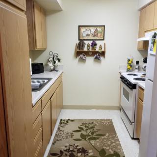 A cozy kitchen with wooden cabinets, a floral rug, and neatly arranged appliances.