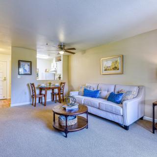 A cozy living room with a sofa, coffee table, and dining area, featuring a ceiling fan and wall art.