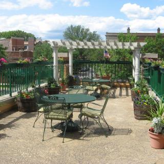 A rooftop patio with garden furniture and greenery under a pergola.