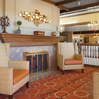 A cozy lobby area featuring a fireplace with two wicker chairs and warm decor.