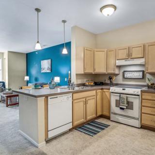 A modern kitchen with an island countertop and wooden cabinets, adjacent to an open living area.