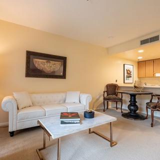 A cozy living room with a white sofa and a marble coffee table, featuring artwork on the wall and an adjacent dining area.