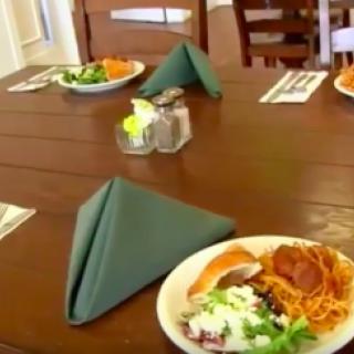A dining table set with plates of spaghetti and salad, accompanied by folded napkins and cutlery.