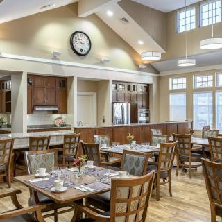 A well-lit dining area with multiple tables and chairs, featuring a large clock on the wall.