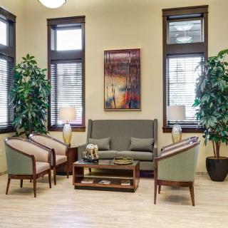 A cozy living room with a sofa, chairs, and a coffee table surrounded by greenery and natural light.