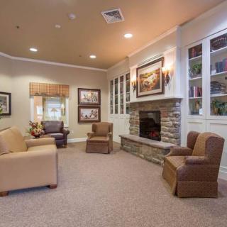 A cozy living room with armchairs arranged around a fireplace, featuring decorative artwork and bookshelves.