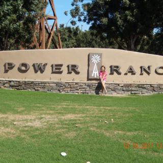 A person standing in front of the Power Ranch sign surrounded by trees and grass.