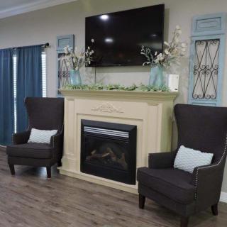 A cozy living room with a fireplace, two armchairs, and a television mounted above the mantel.