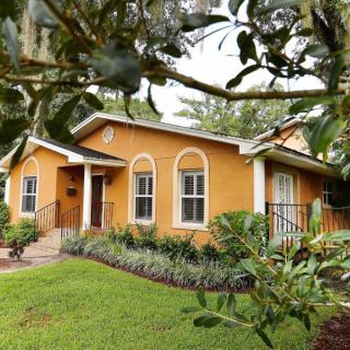 A charming orange house with a well-maintained garden and surrounding trees.