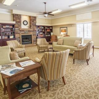 A cozy living room with sofas and armchairs arranged around a fireplace, surrounded by bookshelves and a side table.