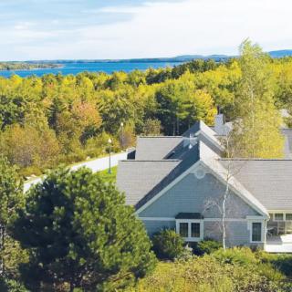 A scenic view of a house surrounded by lush trees and greenery under a clear blue sky.