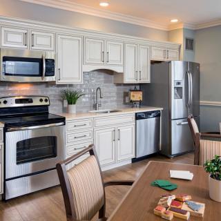 A modern kitchen with white cabinets, stainless steel appliances, and a dining area.