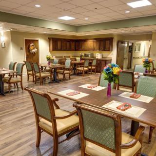 A well-decorated dining room with arranged tables and chairs, featuring flowers as centerpieces.
