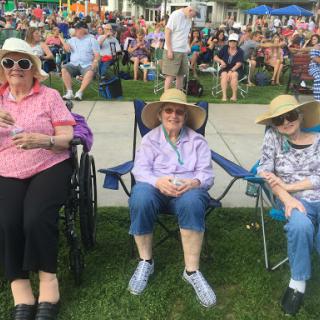 Three elderly women enjoying a sunny day at an outdoor event.