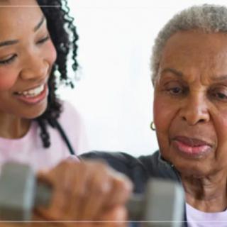 An elderly woman exercises with assistance from a trainer.