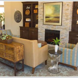 A well-decorated living room featuring a sofa and armchair set around a coffee table, with a fireplace and artwork as focal points.