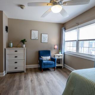 A cozy bedroom with a blue chair, dresser, and large window letting in natural light.