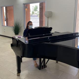 A person wearing a mask plays a grand piano indoors.
