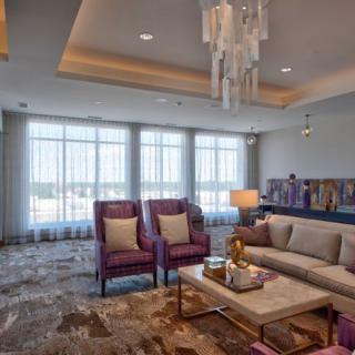 A modern living room with elegant furnishings, featuring a chandelier, plush seating, and ample natural light.