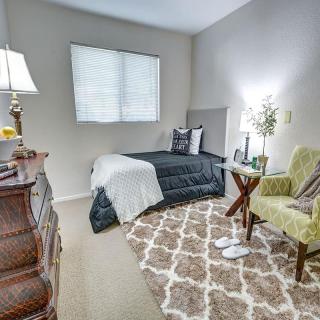 A cozy and well-decorated bedroom with a single bed, armchair, lamp, and patterned rug.