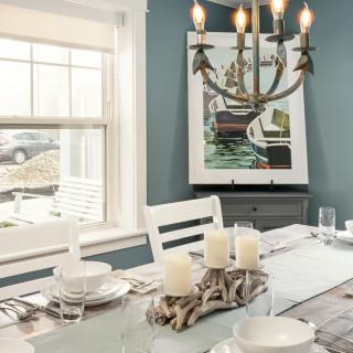 A modern dining room with elegant table settings, a decorative chandelier, and artwork on the wall.