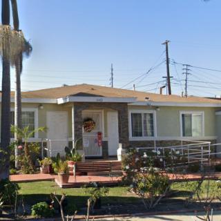 A cozy single-story house with a front porch and ramp, surrounded by a neatly maintained garden on a sunny day.