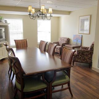 A well-lit dining area with a large wooden table surrounded by chairs, featuring a chandelier and adjacent living space.