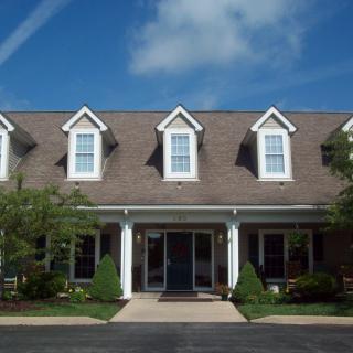 A suburban house with a porch and dormer windows on the roof under a clear blue sky.