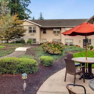 A well-maintained garden patio with seating and an umbrella in front of a building.