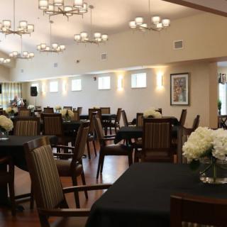 A spacious dining area with neatly arranged tables and chairs, featuring elegant floral centerpieces and ambient lighting.