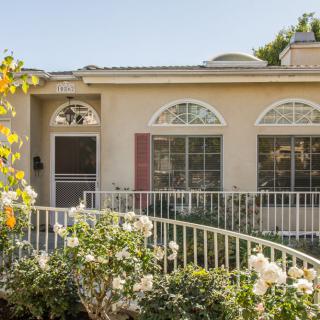 A charming single-story house with large windows and a blooming garden.