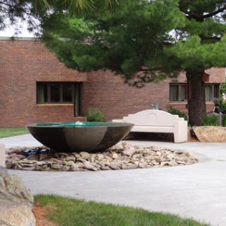 A contemporary fountain surrounded by rocks and greenery in an outdoor setting.