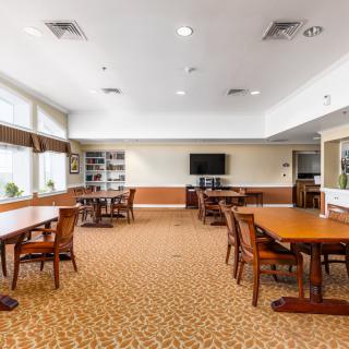 A spacious room with tables and chairs, featuring a television and bookshelves.