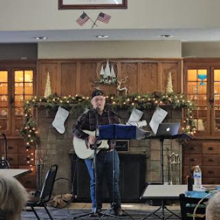 A guitarist performing live in a festive indoor setting, surrounded by holiday decorations.