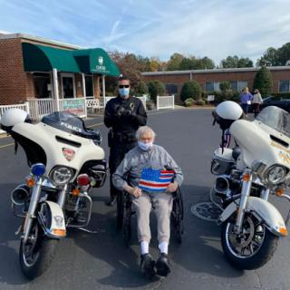 A heartwarming moment as an elderly man enjoys a visit from police officers by their motorcycles outside a healthcare facility.