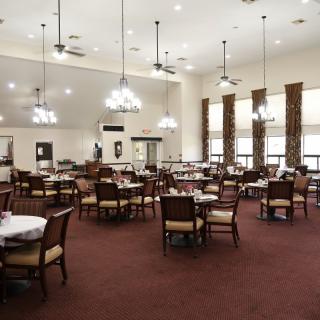 A spacious dining hall with elegant chandeliers, carpeted flooring, and neatly arranged tables and chairs.