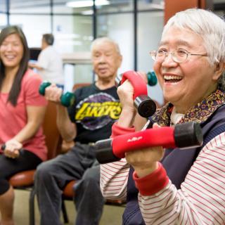 A group of seniors participating in a fitness class, smiling and lifting dumbbells.