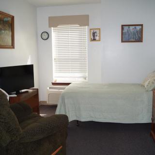 A bedroom with a bed, television, and a comfortable chair.