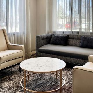 A modern living room featuring a gray sofa, beige armchairs, and a round marble-topped coffee table.