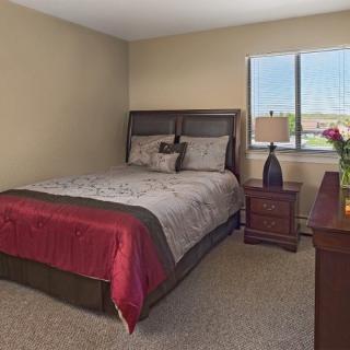 A cozy bedroom with a neatly made bed, bedside table, and window view.