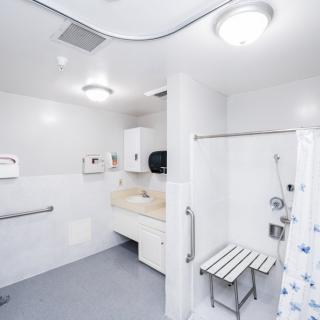 A modern, accessible bathroom featuring a shower with a chair and grab bars.