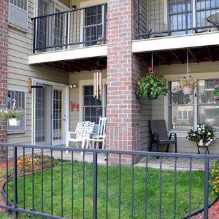 An apartment with balconies and a small fenced lawn, featuring outdoor seating and hanging plants.